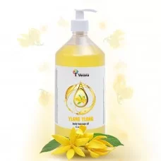Fles Verana Ylang Ylang massageolie met ylang-ylang bloemen op de achtergrond.